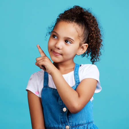 Thats what I want. Shot of an adorable little girl pointing at something while standing against a blue background.の写真素材