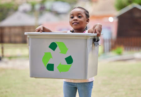 Taking care of the environment. Shot of a little girl carrying a recycling box outside.