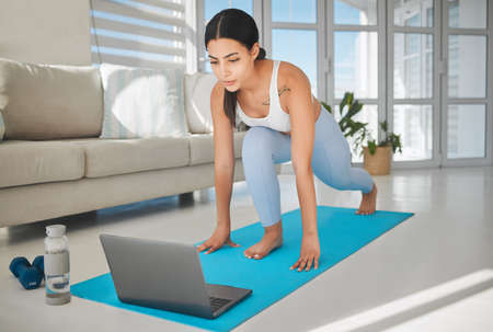Virtual workouts are great to do in your own time. Shot of a sporty young woman using a laptop and...