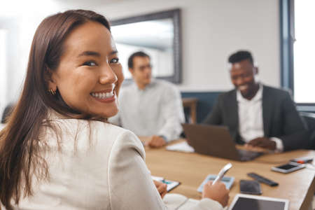 Portrait of a young asian business woman smiling while sitting in the boardroom during a meeting with her colleagues. A team talking strategy and planning for success. Theres a new girl boss in townの写真素材