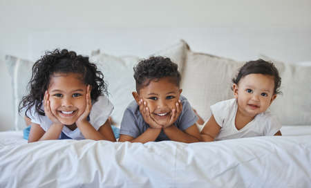 Brothers and sisters are as close as hands and feet. Shot of three siblings lying together in bed.の写真素材