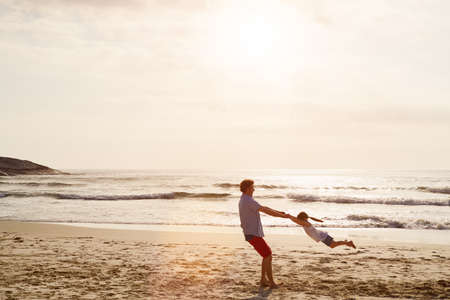 Experiencing the joys of life. Shot of a father swinging his daughter around at the beach.の写真素材