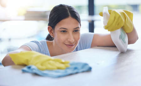 Shot of a young woman smiling while cleaning a surface at home.