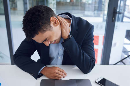Stressed out and feeling it. Shot of a young businessman experiencing neck pain while working in an office.の写真素材