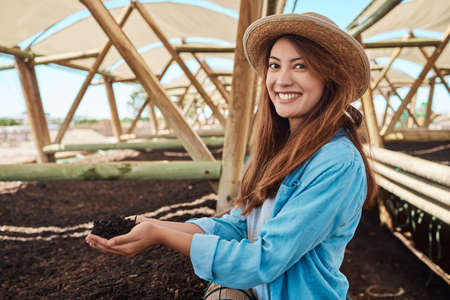 This soil is optimum for growing healthy crops. Portrait of a young woman holding soil in her hands while working on a farm.の写真素材