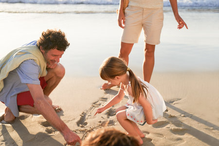 The beach holds so many secrets. Shot of a family drawing shapes in the beach sand together.の写真素材