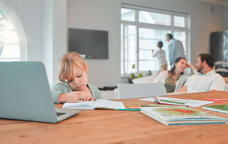 Serious young little girl writing in a notebook doing her home work while sitting at a table in the...