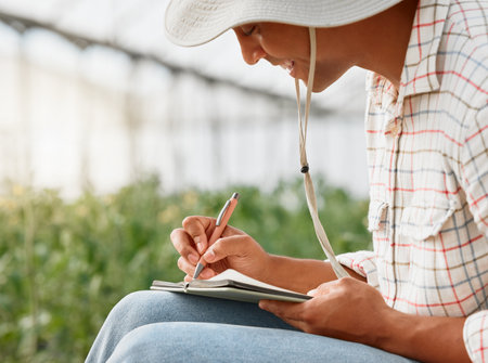 Shot of a young man writing notes while working in a greenhouse on a farm.の写真素材