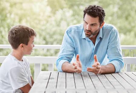 Shot of a young father and son talking outside in the garden at home.の写真素材