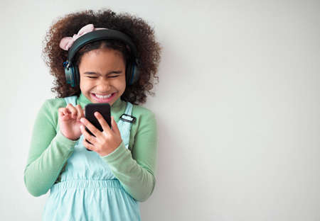 Heaven in her eye. Shot of an little girl using a phone and listening to music through headphones against a grey background.の写真素材