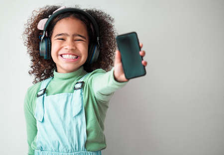 In every gesture, dignity and love. Shot of an little girl standing alone e and listening to music through headphones against a grey background.の写真素材