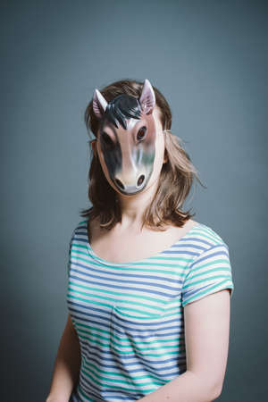 Young woman wearing mask against a grey background in studio. Young woman wearing mask against a grey background in studio.の写真素材