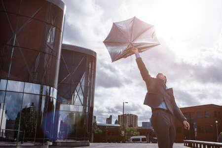 Life hasnt been kind lately. Shot of a businessman holding an umbrella being broken by the wind.の写真素材
