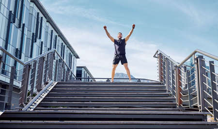 Low angle shot of a sporty young man cheering at the top of a staircase while exercising outdoors.