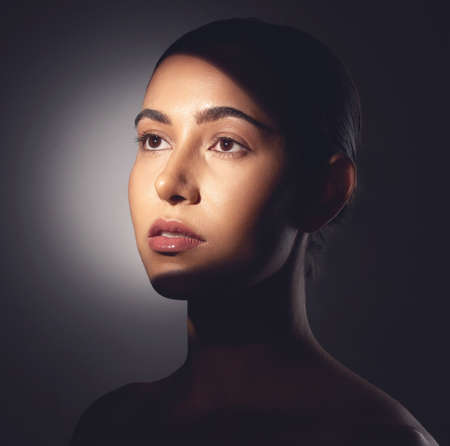 A major component of healthy skin is a natural glow. Studio shot of a beautiful young woman posing with light beam against her face.の写真素材
