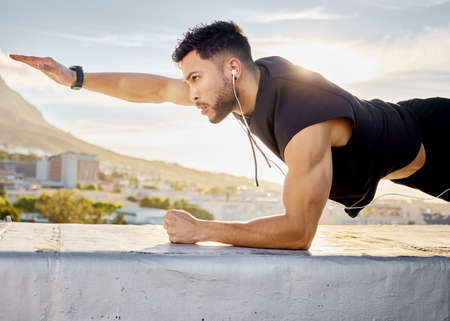 Just keep pushing forward. Shot of a man doing a single-arm plank while on a rooftop.の写真素材