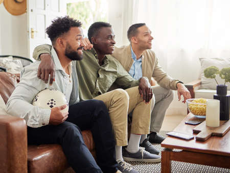 Its game day and we just had to get together for it. Shot of three male friends watching something together while sitting on a couch.の写真素材