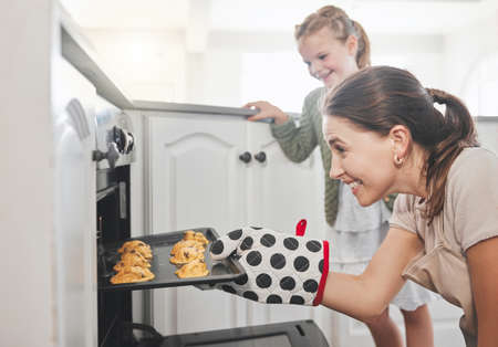 Thats the art of baking. Shot of a mother and daughter putting a tray of cookies in the oven at home.の写真素材