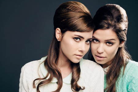 She is me and I am her. Studio shot of two attractive young women dressed up in 60s wear against a...
