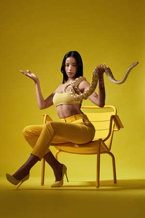 We could do it my way or we can do it the other way. Shot of a fashionable woman holding a snake while modelling a yellow concept.の写真素材