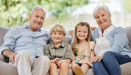 Portrait of an affectionate family of four sitting comfortable on their sofa in the living room at home. A grandmother, grandfather, grandson and granddaughter enjoying quality time together and bonding. Every grandparent wants the best for their grandchildren. Senior caucasian couple spending time with their grandchildren.の写真素材