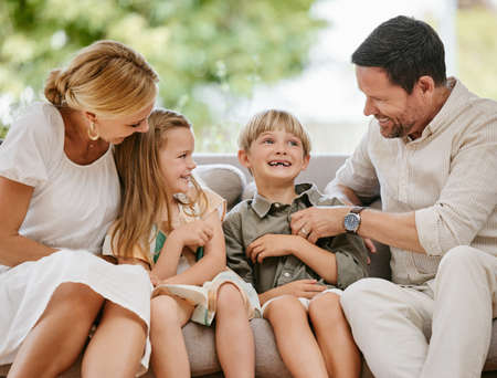 Affectionate family of four sitting on their sofa in the living room at home. A mother, father, son and daughter enjoying quality time together and bonding. Every parent wants the best for their kidsの写真素材