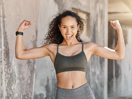 Shot of an attractive young woman standing alone and flexing her muscles during her outdoor workout...
