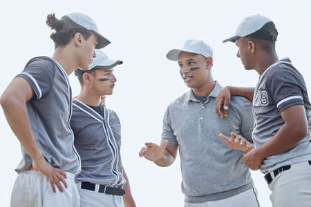 Baseball coach from below giving match pep talk and planning game strategy with group of players in huddle on sports pitch outside. Trainer encouraging and motivating team for tournament competitionの写真素材