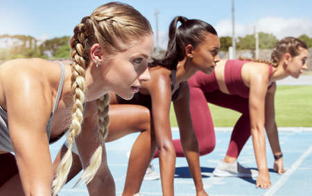 Three female athletes at the starting line in a track race competition at the stadium. Young sporty...