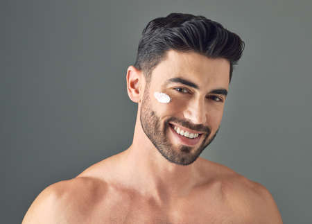 I keep my moisture barrier in good shape. Studio shot of a handsome young man posing with moisturiser on his face.の写真素材