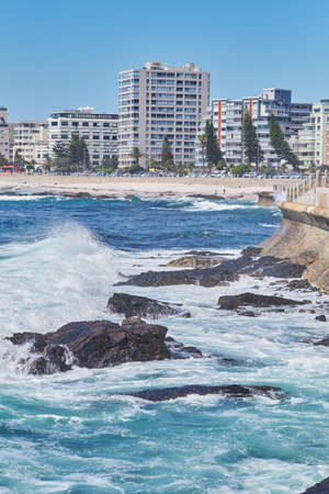 Rocky sea near city housing. Tall apartment buildings beside a beach on a sunny day. A popular...