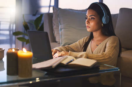 Cramming before the exam. Cropped shot of an attractive young woman working late at night in her living room at home.の写真素材