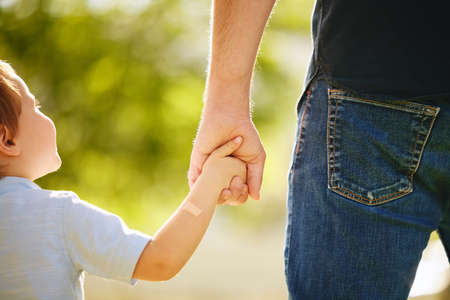 Hell always have a hand to hold. Shot of a little boy holding his dads hand on a walk in the park.の写真素材