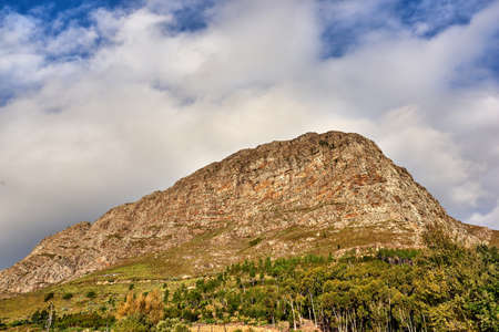 A bottom view picture of Table mountain. A beautiful nature view of a high mountain shaped like a lions head with forest, and a cloudy sky in the background. Copy space with scenic landscape viewの写真素材