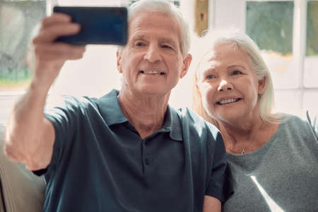 A selfie for the kids. Cropped shot of an affectionate senior couple sitting in their living room at...