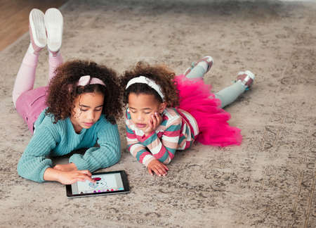 Getting colourful and creative. High angle shot of two little girls playing on a digital tablet together at home.の写真素材