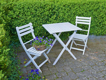 Two courtyard chairs and table in a secluded and private garden at home. Wooden patio furniture and...
