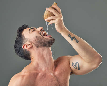 Its an all-natural way to hydrate. Studio shot of a man drinking coconut water.
