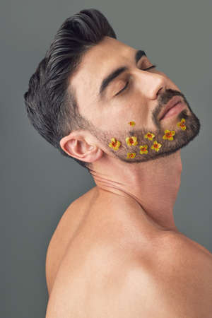 Want to grow a more fuller beard. Studio shot of a handsome young woman posing with flowers in his beard.の写真素材