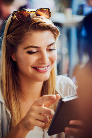 Beautiful caucasian woman smiling while using her smartphone in a cafe. Woman wearing sunglasses on...