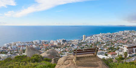 Beautiful aerial landscape of an ocean in Sea Point, Cape Town, South Africa. A calm summer day with a park bench overlooking hotels and a suburban housing area in a beautiful blue seascapeの写真素材