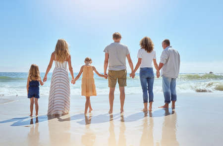 Rear view of family holding hands and having fun on a beach vacation together on a sunny day. Relatives enjoying summer and sunshine, bonding and spending quality time walking and feeling ocean waterの写真素材