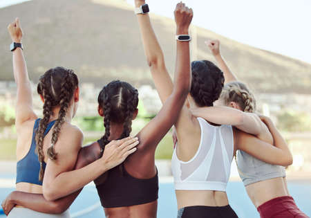 Rear view of proud excited Olympic champions hugging and cheering together in unity. Active young team rejoicing after winning an achievement. A group of diverse female athletes celebrating victory.の写真素材