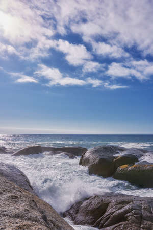 Rocks in the ocean under a blue cloudy sky with copy space. Scenic landscape of beach waves...