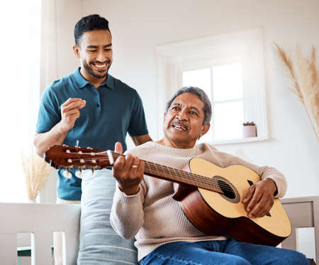 Nothing sweeter than the sound a guitar makes. Shot of a young man listening to his father play the guitar at home.の写真素材
