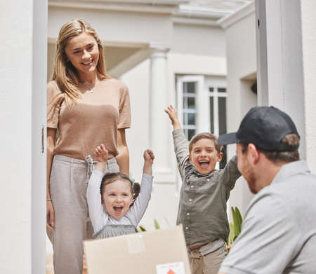 Yay. Cropped shot of two adorable little kids cheering while a male courier delivers a package to their mom.の写真素材