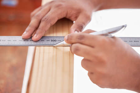 Im cutting off the rest. Cropped shot of a carpenter doing measurements on wood.の写真素材