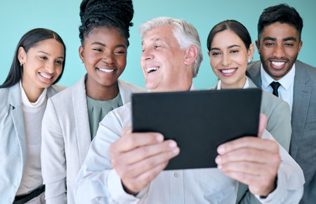 Thats an awesome picture. Studio shot of a diverse group of corporate businesspeople using a tablet to take selfies against a blue background.の写真素材