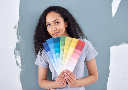 What color can I add to compliment this one. Shot of a woman holding up color swatches while standing against a painted wall.の写真素材