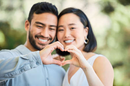 With you, my heart is whole. Shot of a happy young couple making a heart shaped gesture in a garden.の写真素材